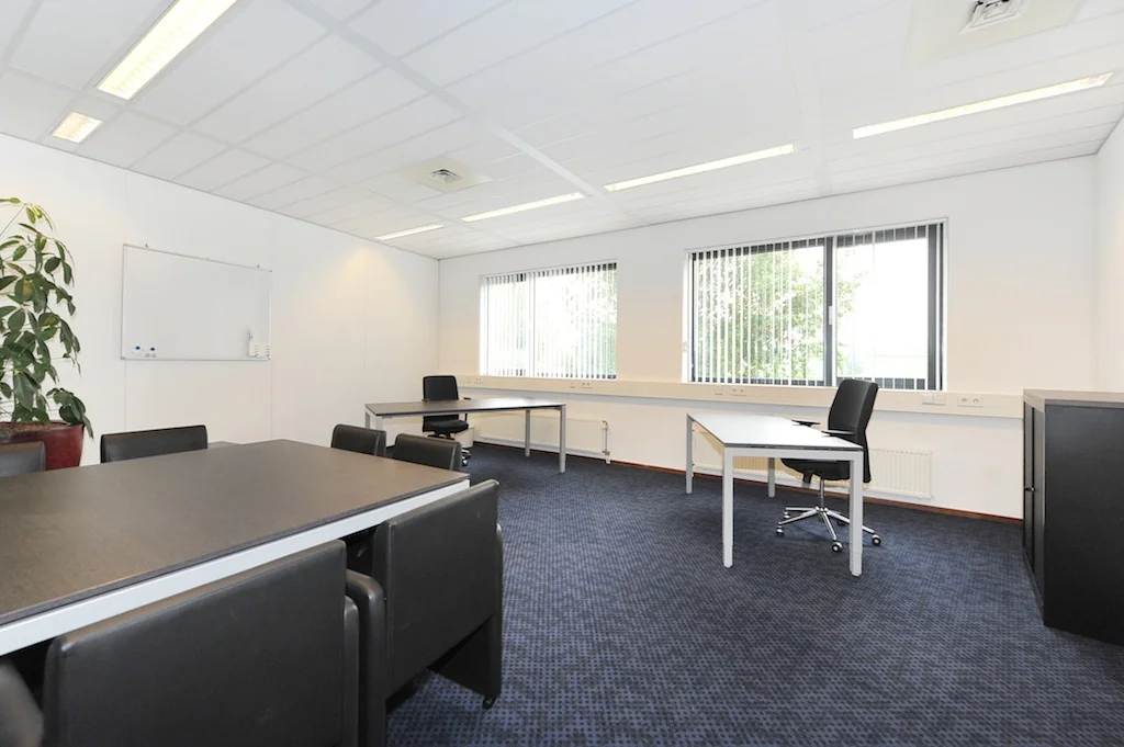 Moderne, lichte kantoorruimte aan de Laan van ’s-Gravenmade met werkplekken, vergadertafel en grote ramen met lamellen.